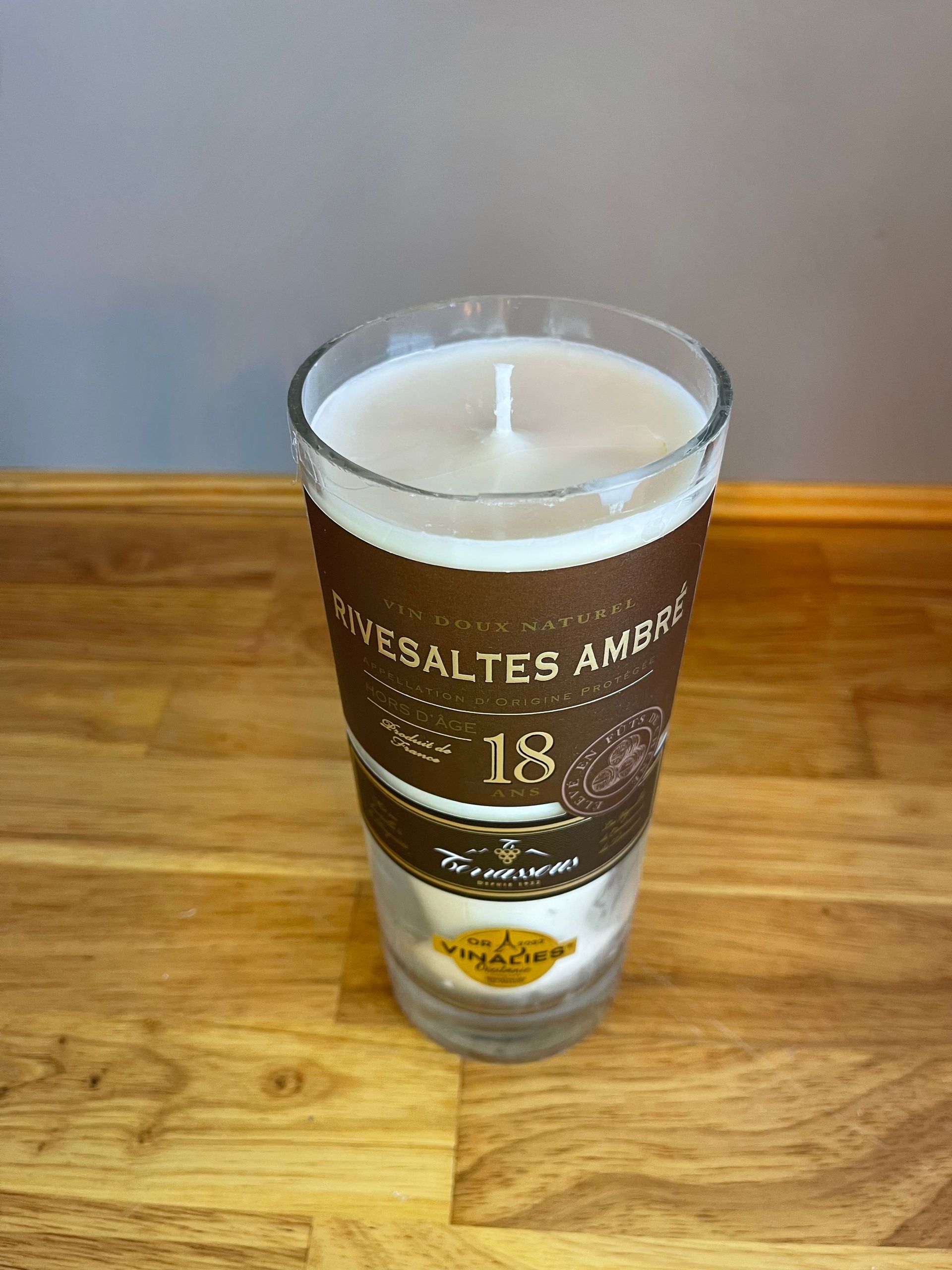 Clear shot glass with brown label and gold text on a wooden table against a gray background