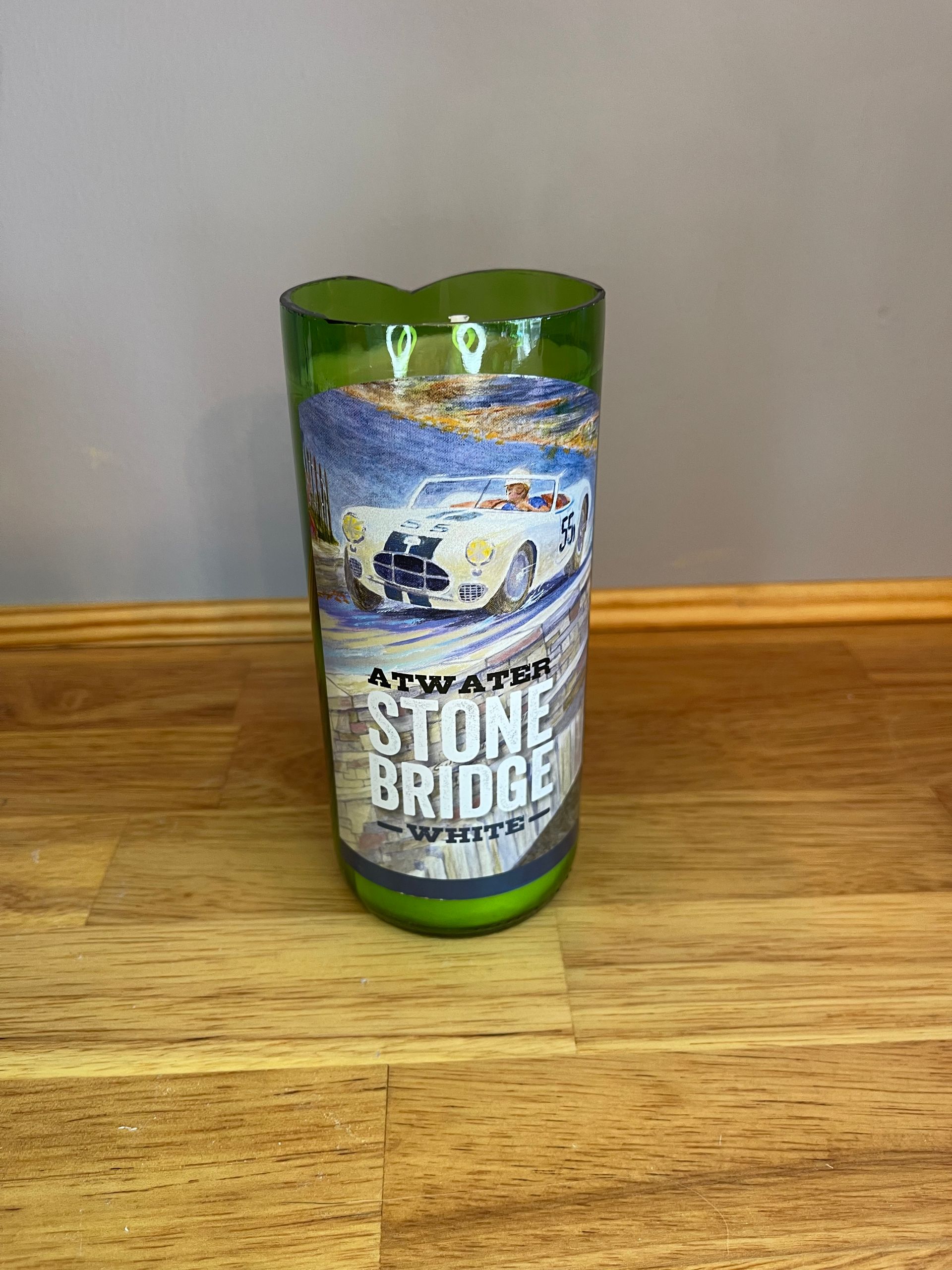 Green glass candle holder labeled “Stone Bridge” on a wooden table.