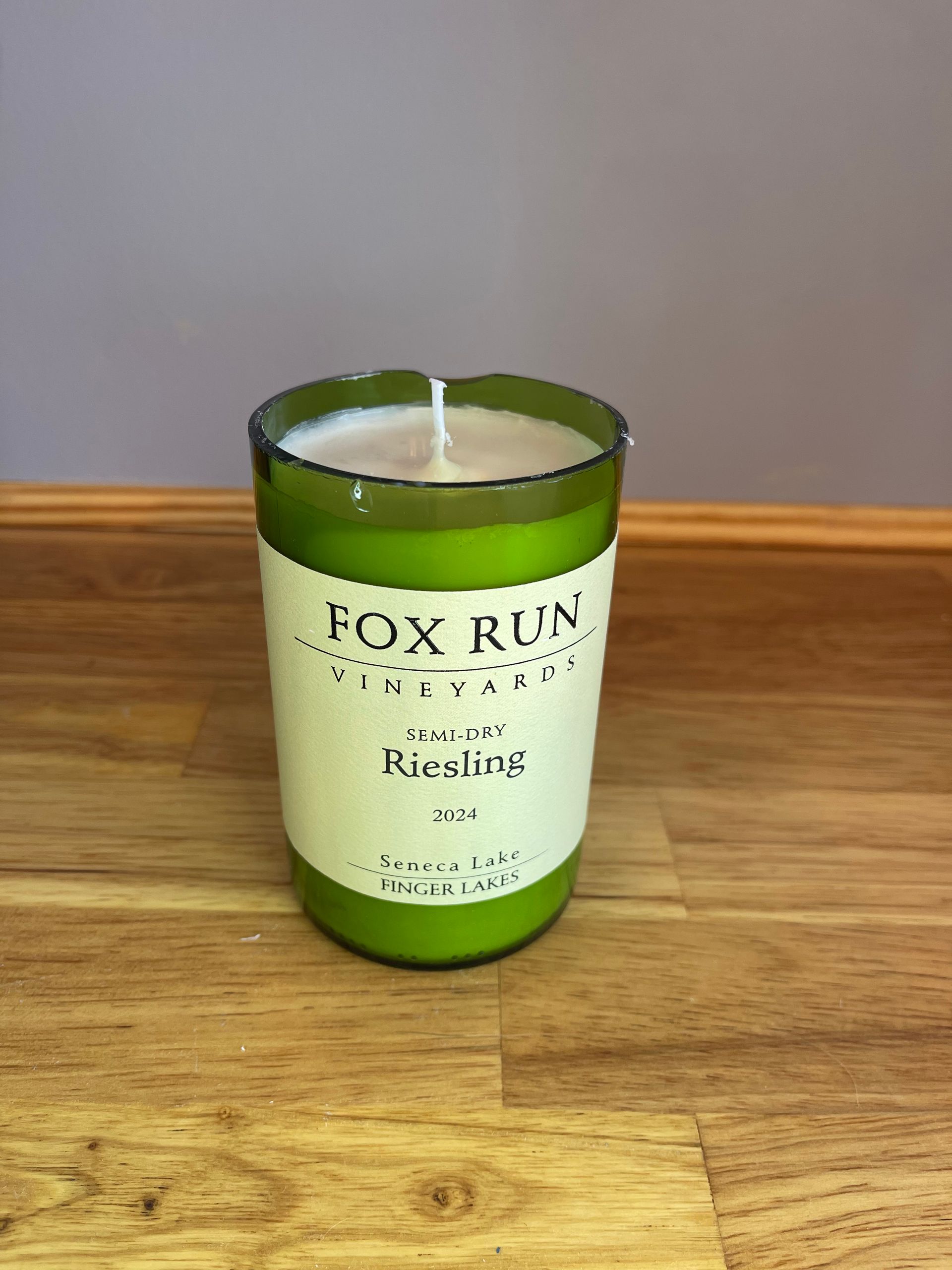 Green glass candle jar with white wax and visible wick on a wooden table
