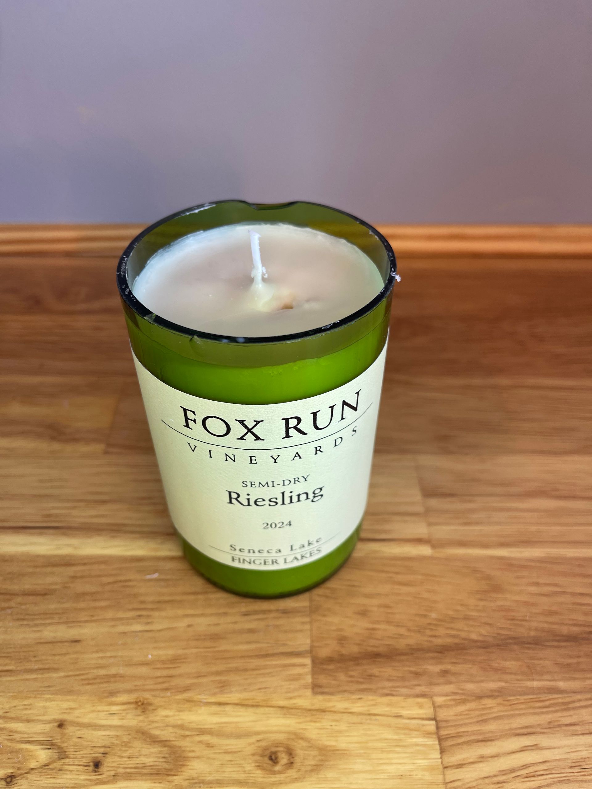 Green glass candle jar with white wax and visible wick on a wooden table