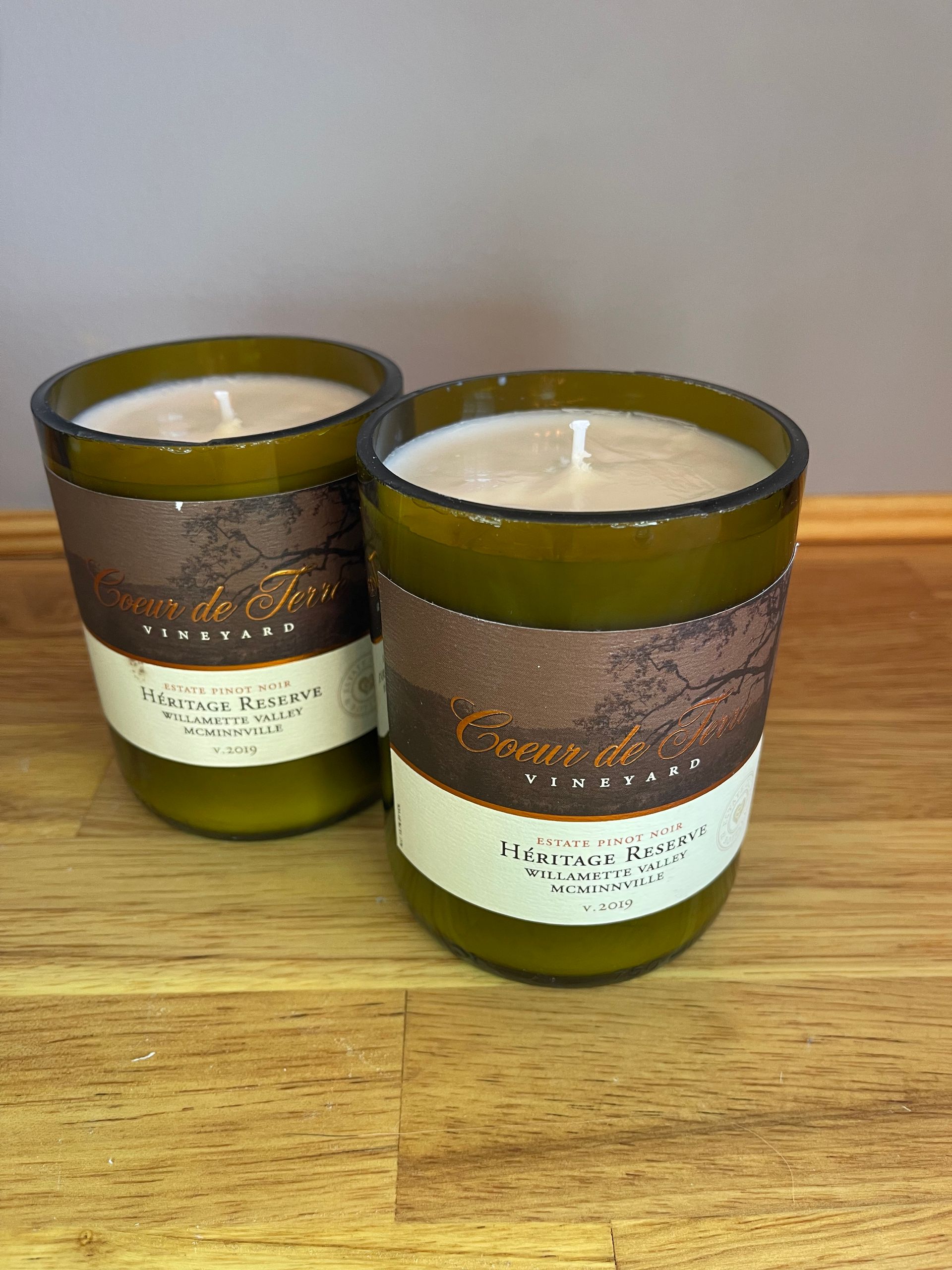 Two brown-and-green scented candles on a wooden surface