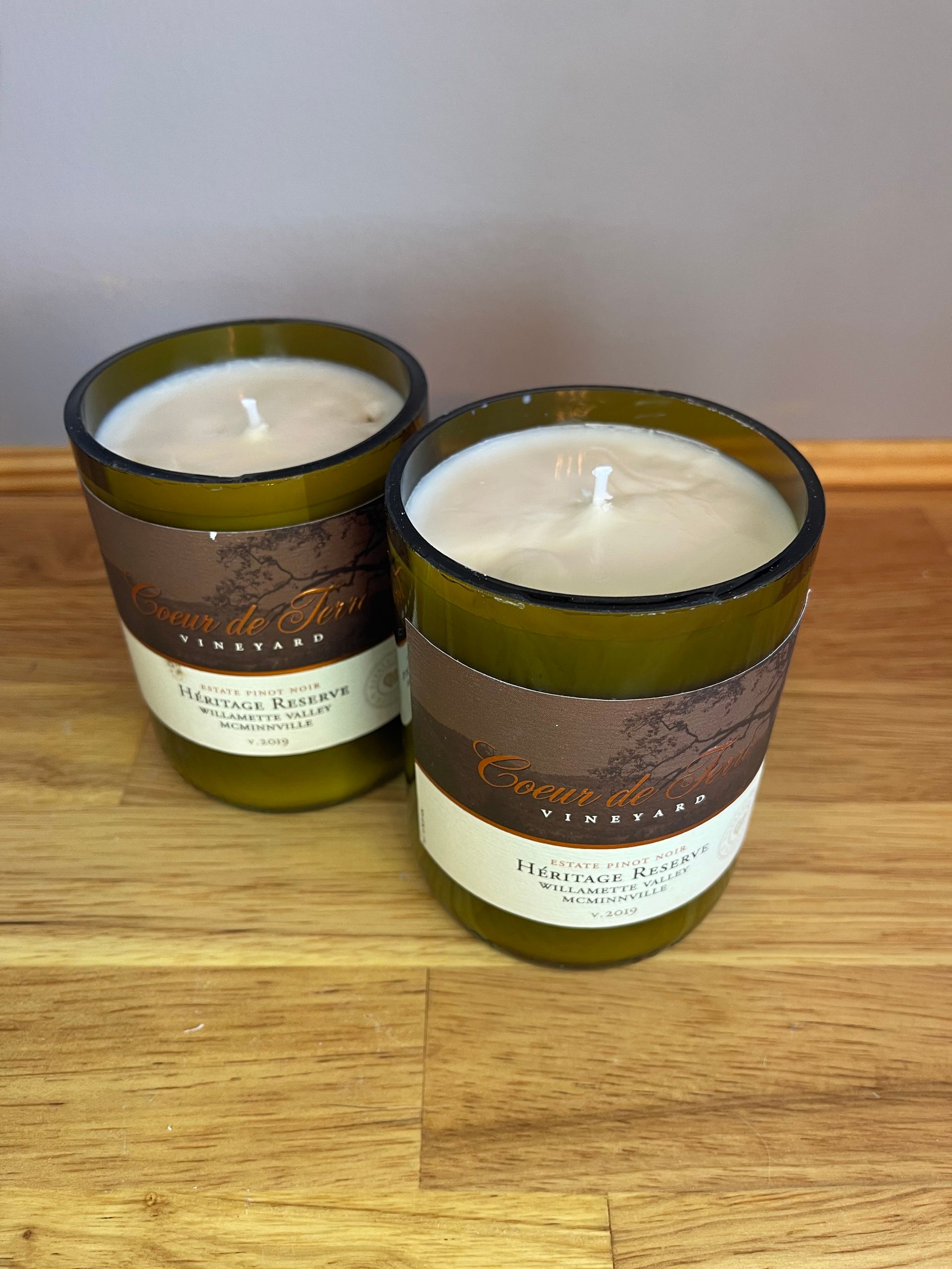 Two brown-and-green scented candles on a wooden surface