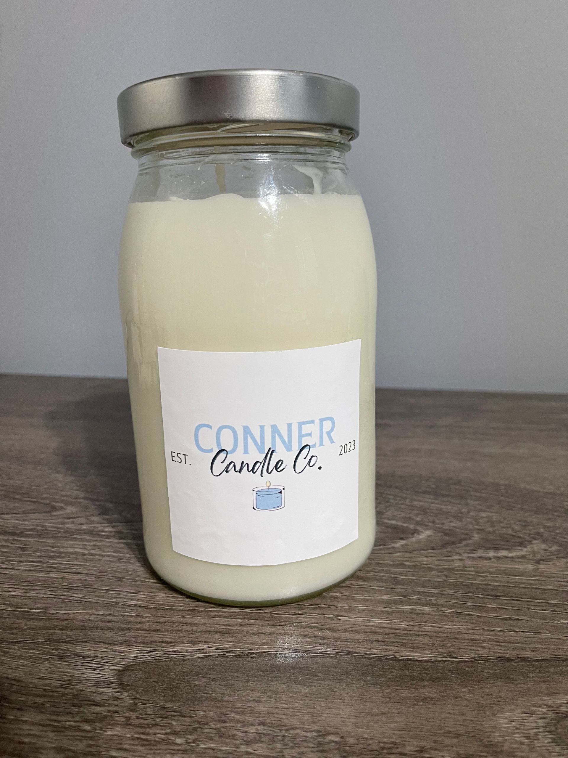 Jar candle with a label that says "Conner Candle Co." sits on a wooden surface.