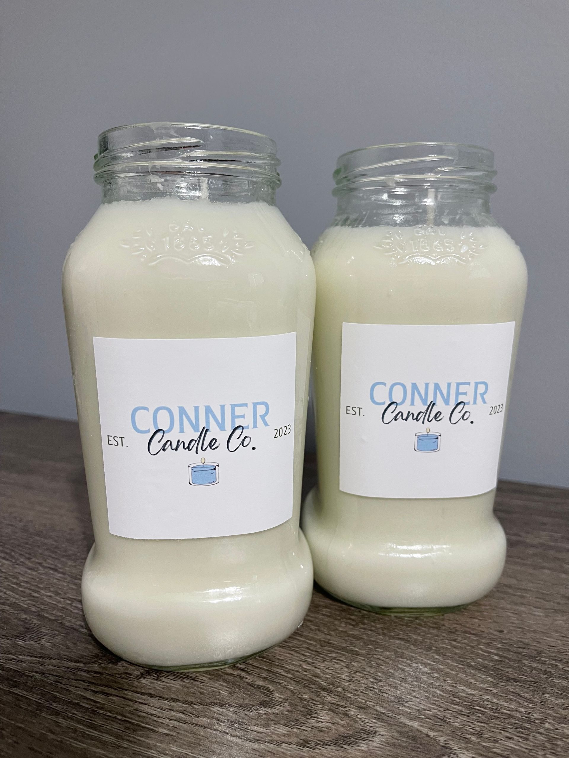 Two white candle jars with "Conner Candle Co." labels on a gray surface.