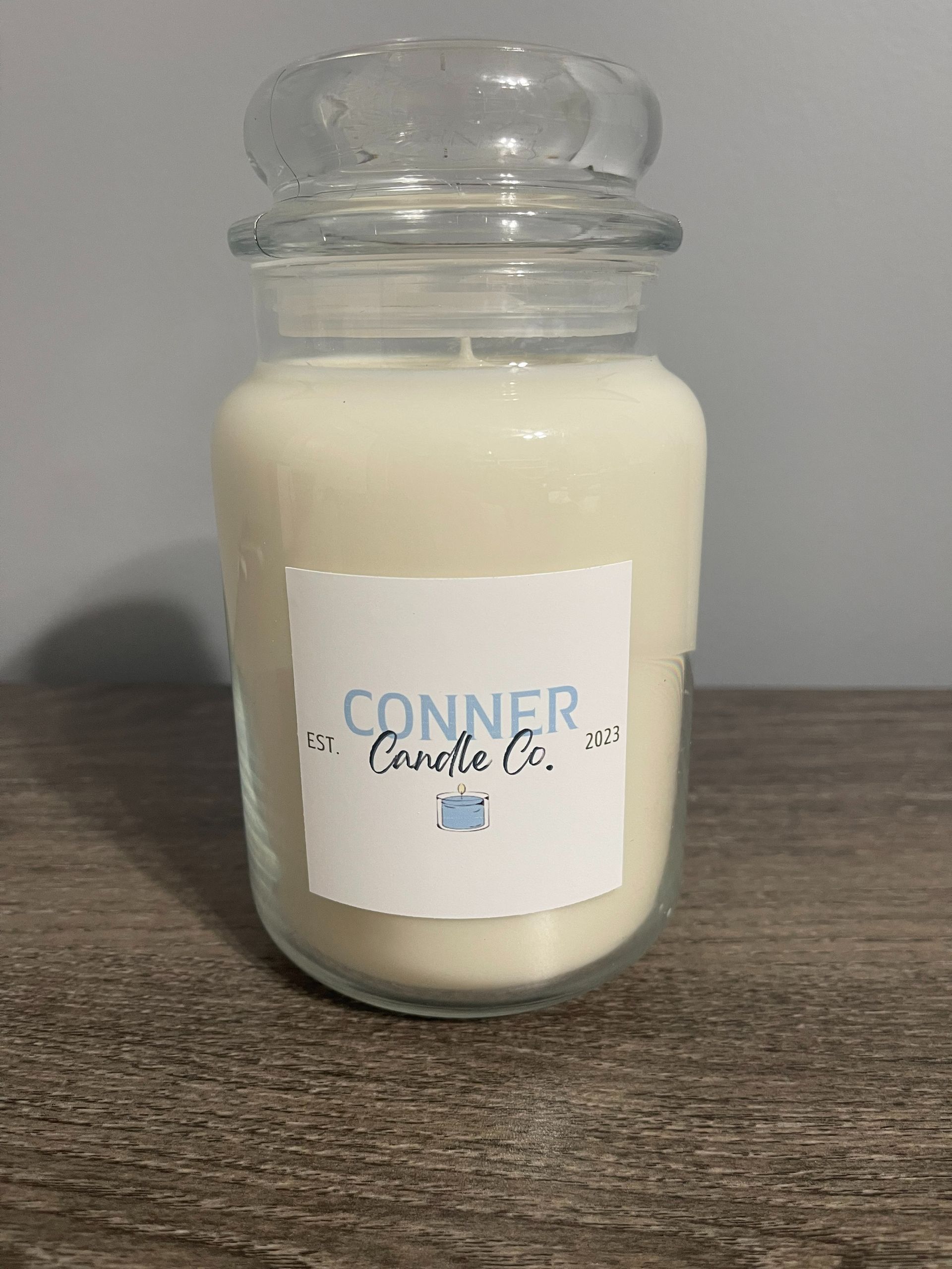 White candle in a glass jar with a clear lid, label reads "Conner Candle Co."