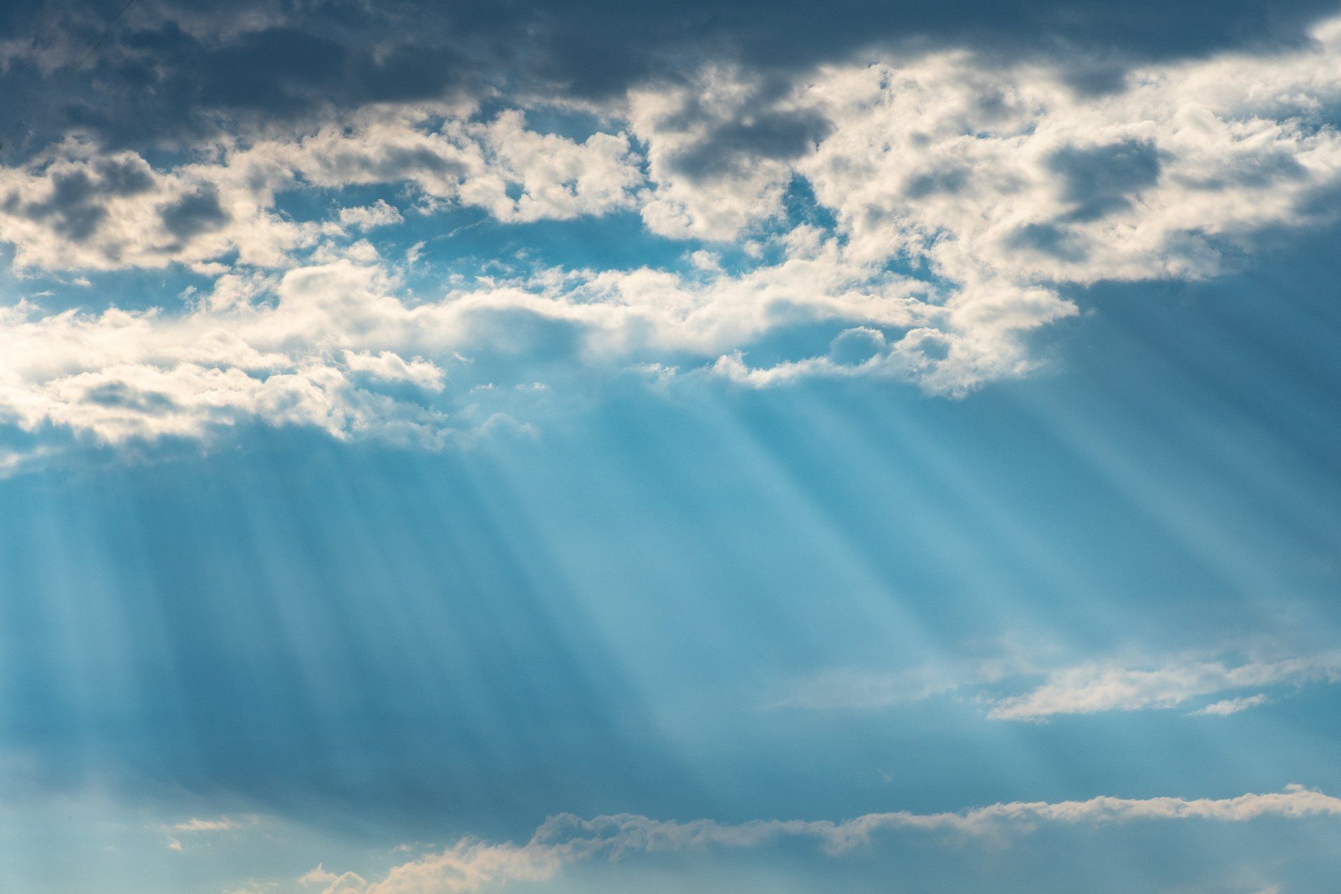 Blue sky with fluffy white clouds, sun rays shining through.