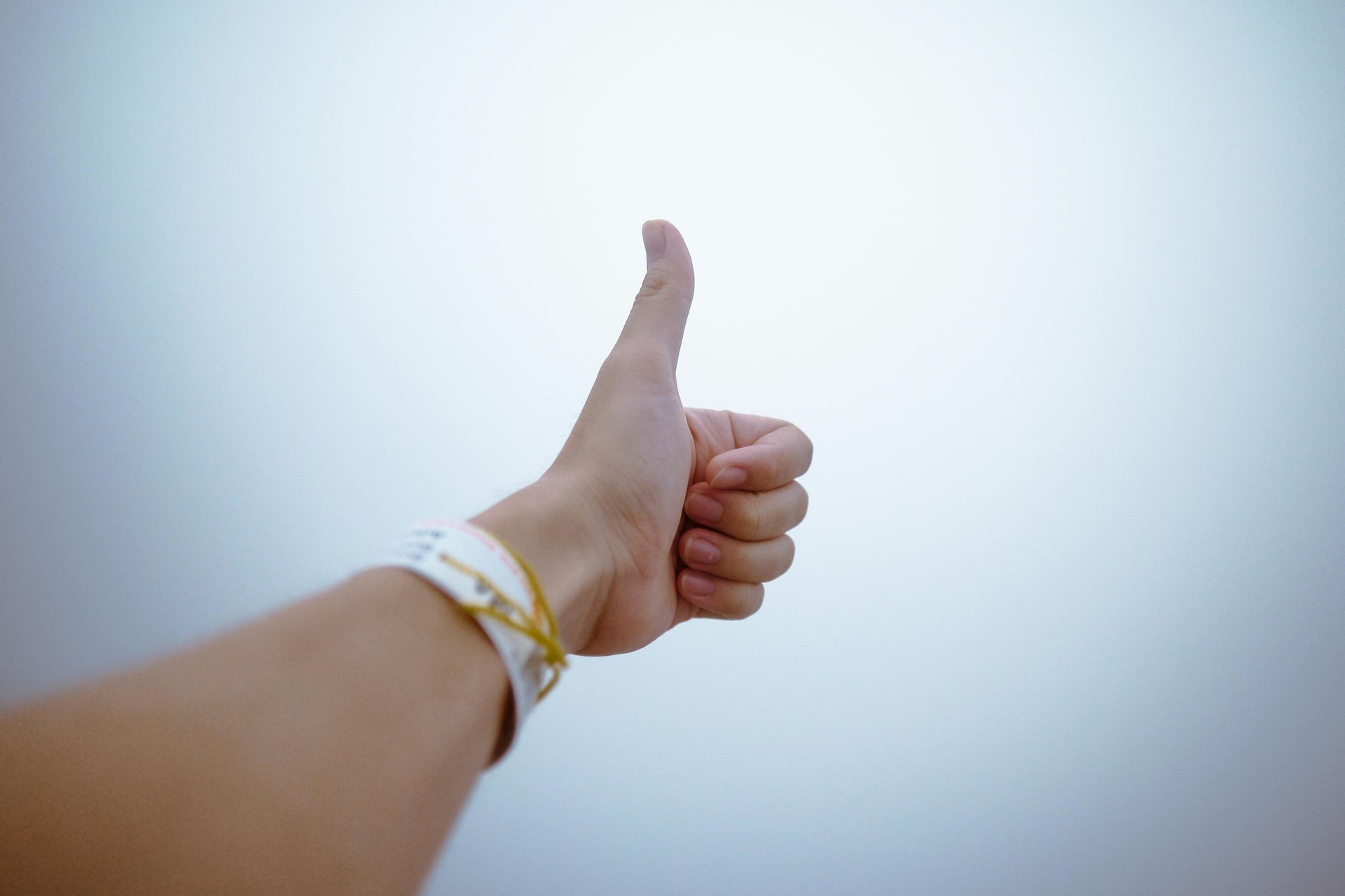 Hand with thumb up against a gray background, wearing a white and gold bracelet.
