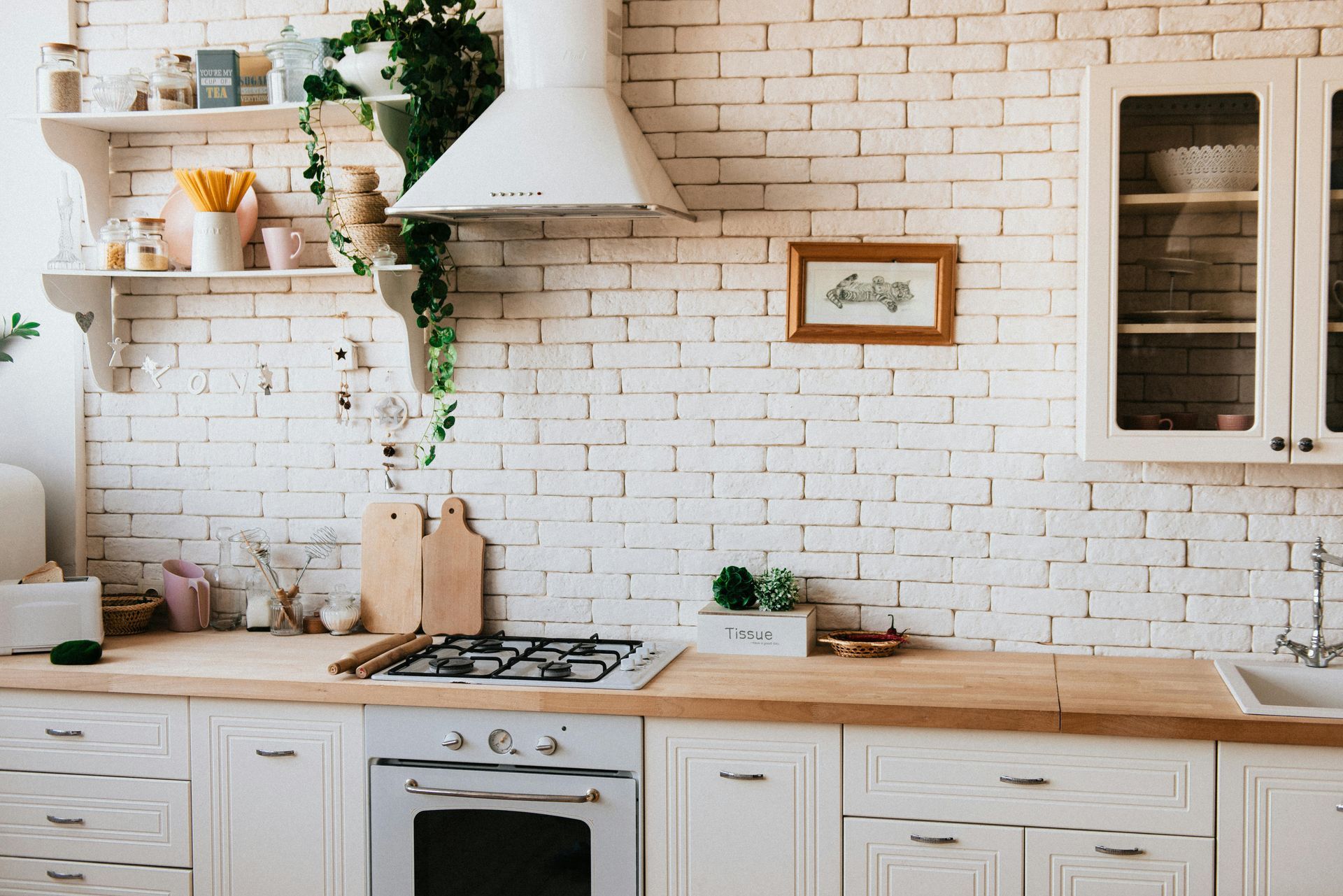 White kitchen with exposed brick wall, wooden countertops, and white cabinets.