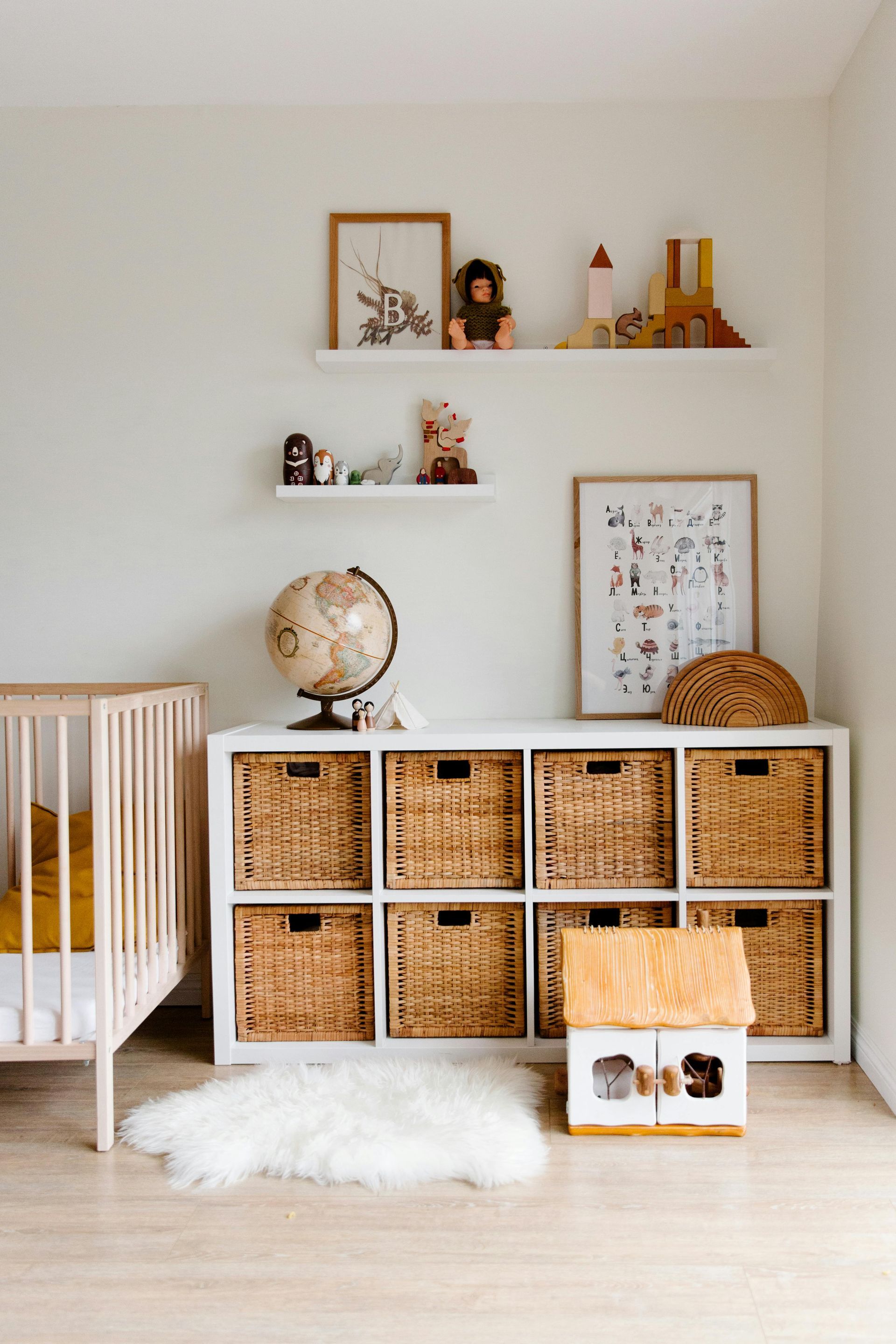 A nursery with a crib, storage cube with woven baskets, shelves with toys, and a globe.