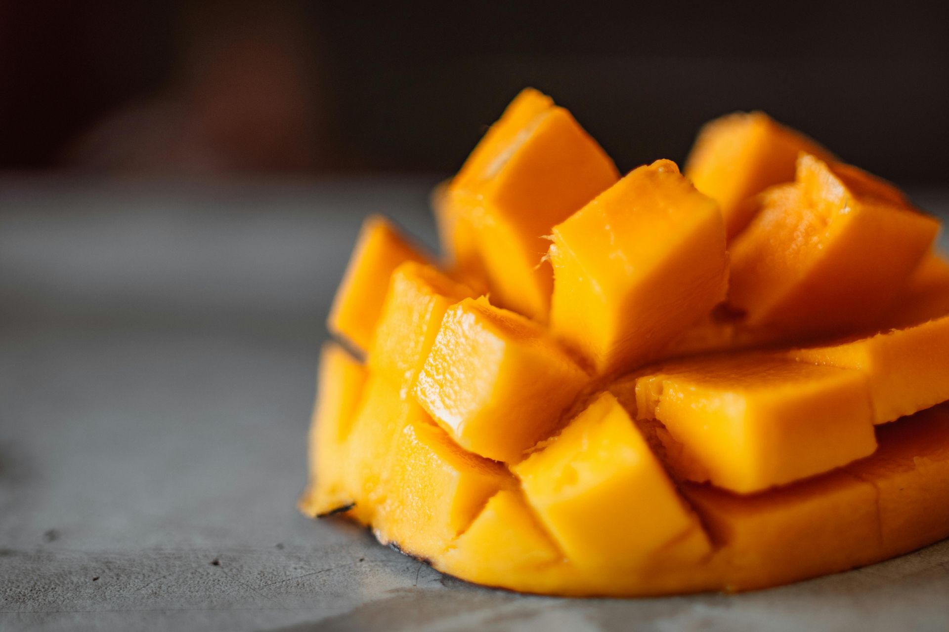 Diced mango fruit, bright yellow, on a gray surface.