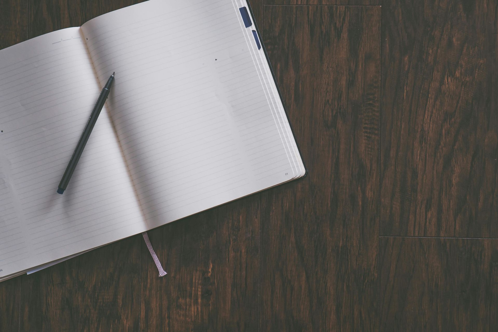 Open notebook and pen on a dark wood surface, ready for writing.