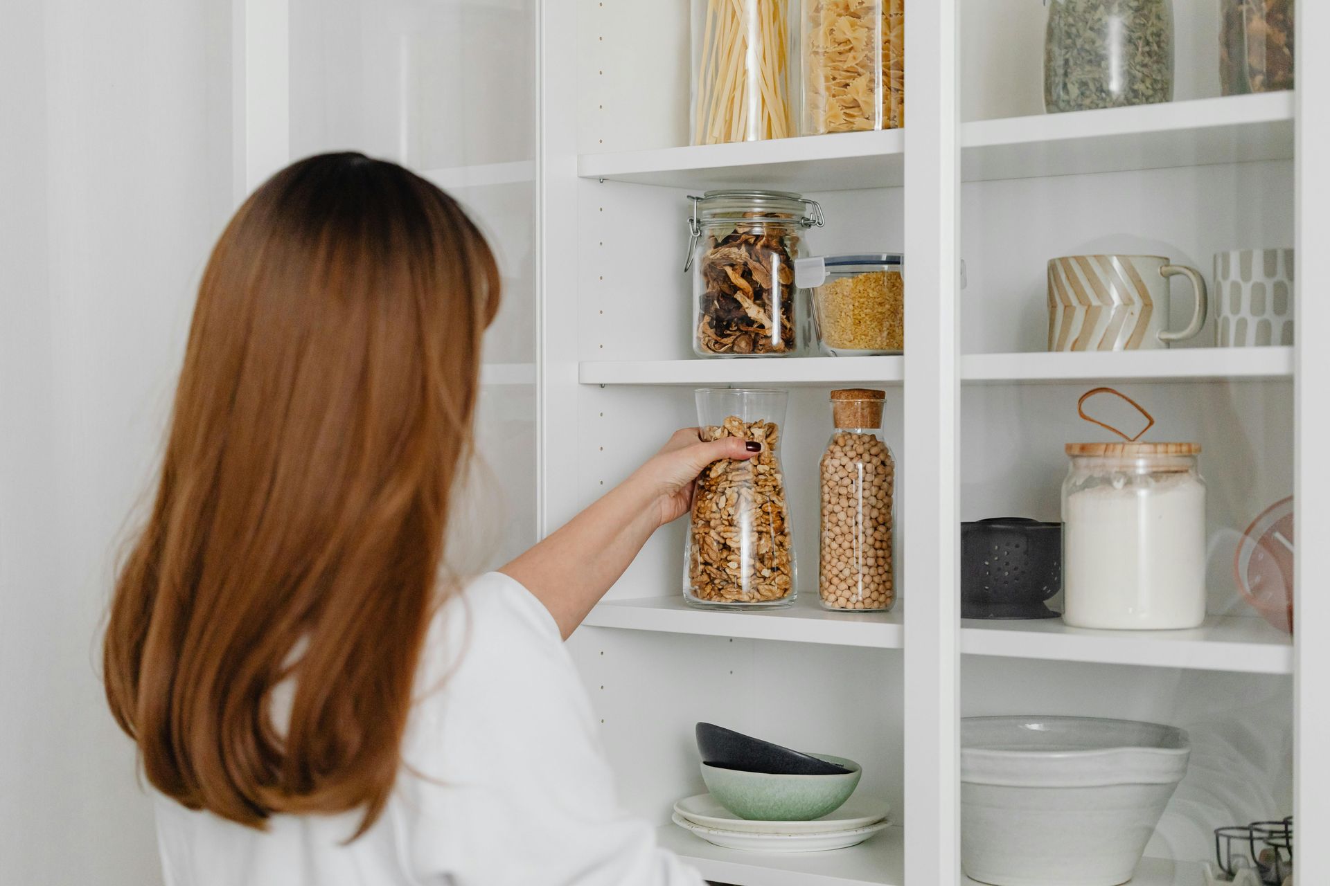 Woman reaching into a pantry shelf to grab a jar filled with food.
