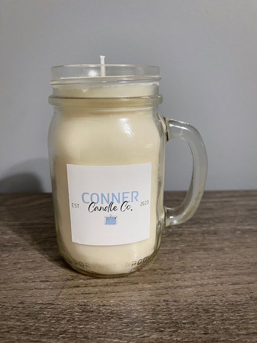 Candle in a mason jar with a handle, labeled "Conner Candle Co." on a wooden surface.