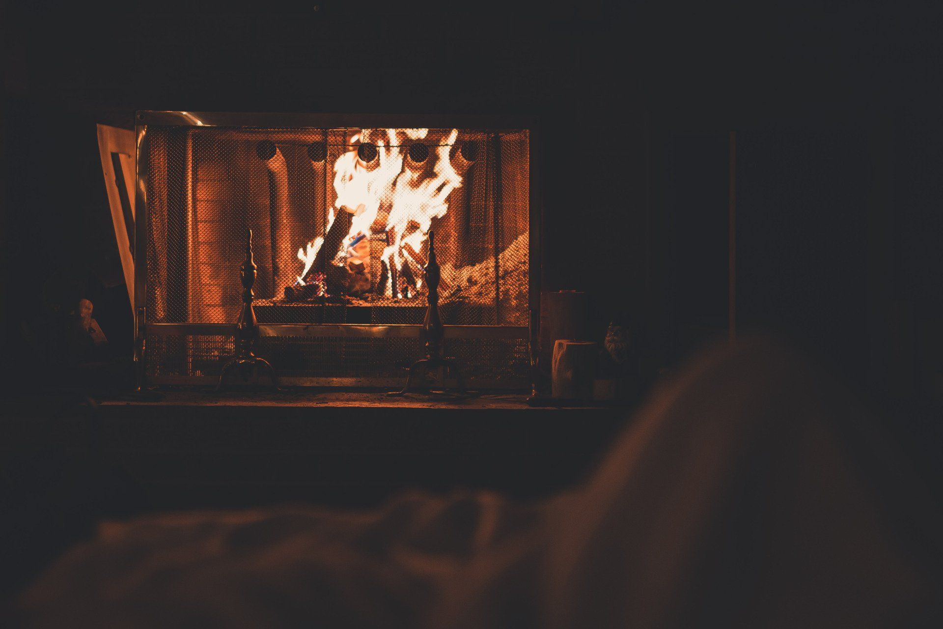Fire burning brightly in a fireplace, casting an orange glow in a dimly lit room.