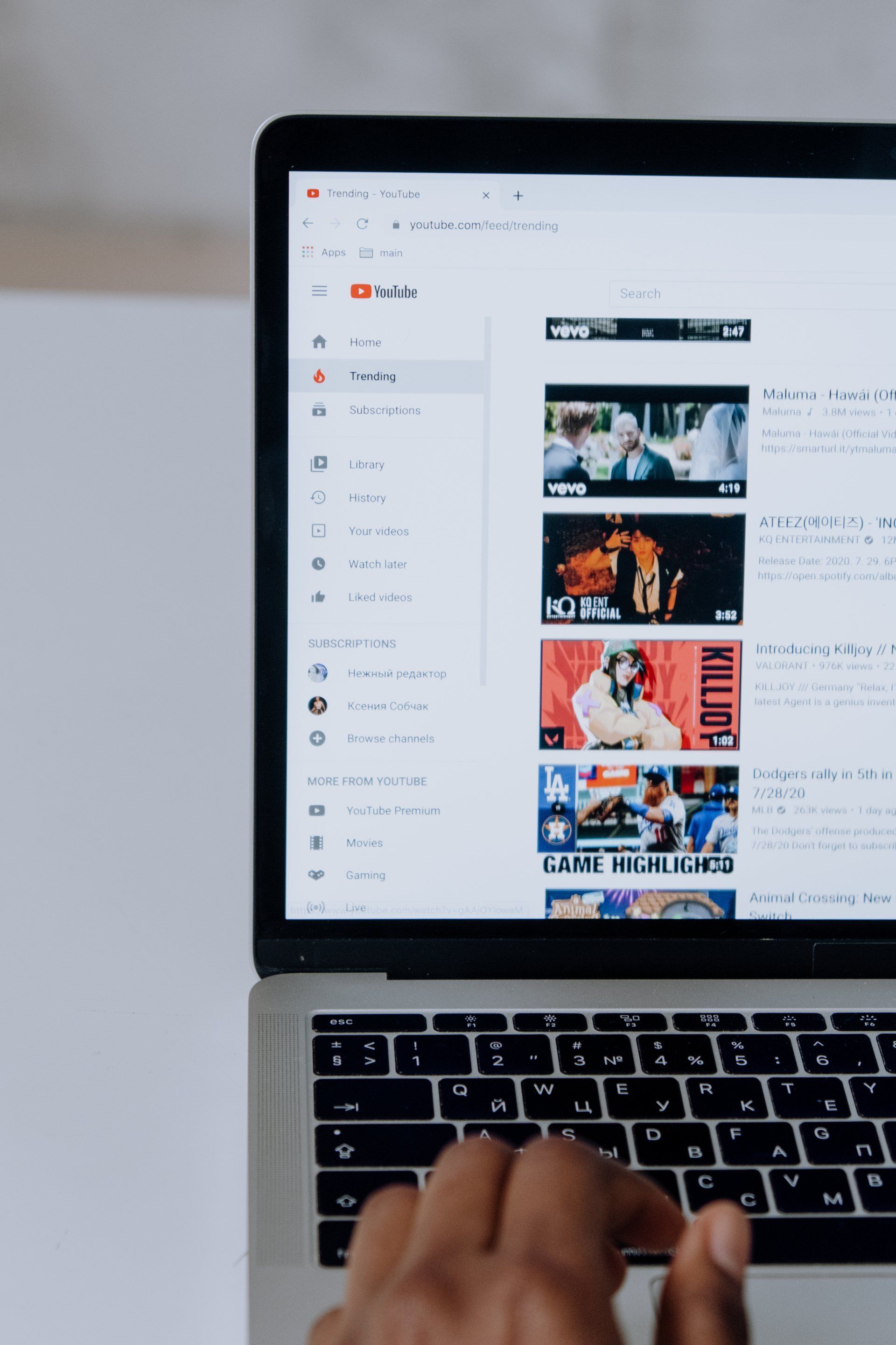 Laptop displaying YouTube website, black hand typing on keyboard.