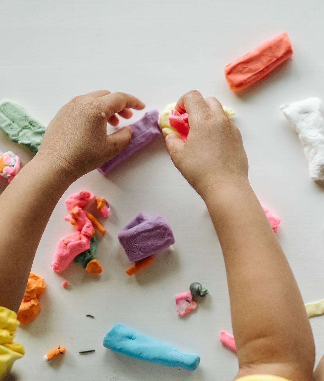 Hands playing with colorful playdough on a white surface.