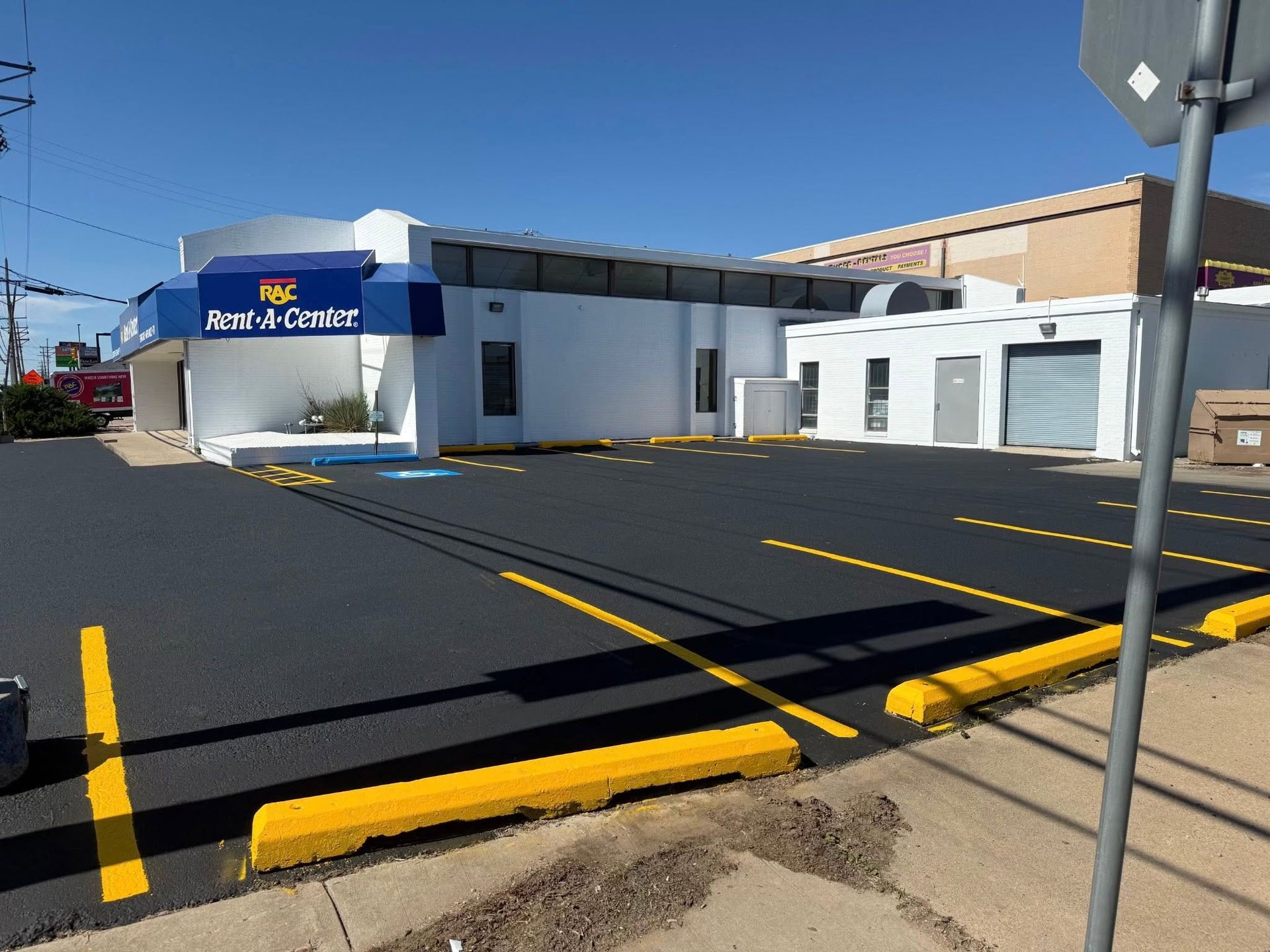Blue-and-white building with a bank sign, parking lot, and yellow curb under clear sky
