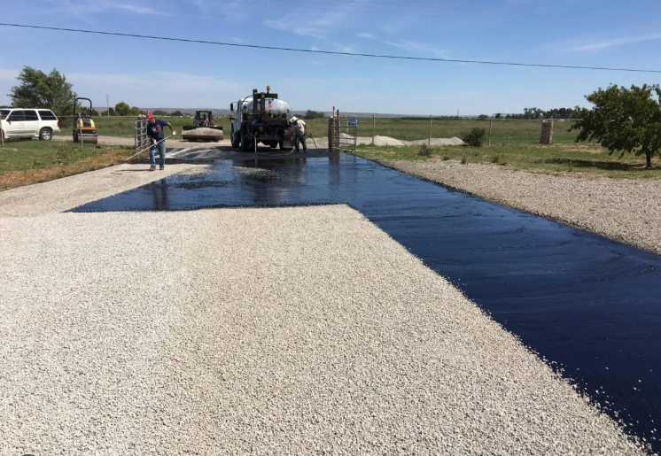 Construction site with asphalt paving machine laying dark pavement over gravel road