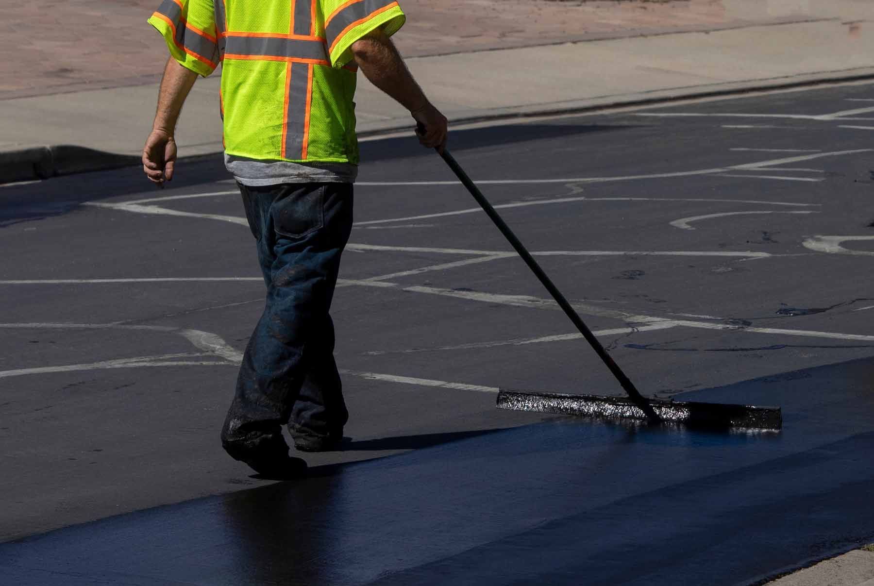 A man is walking down a street sealing asphalt
