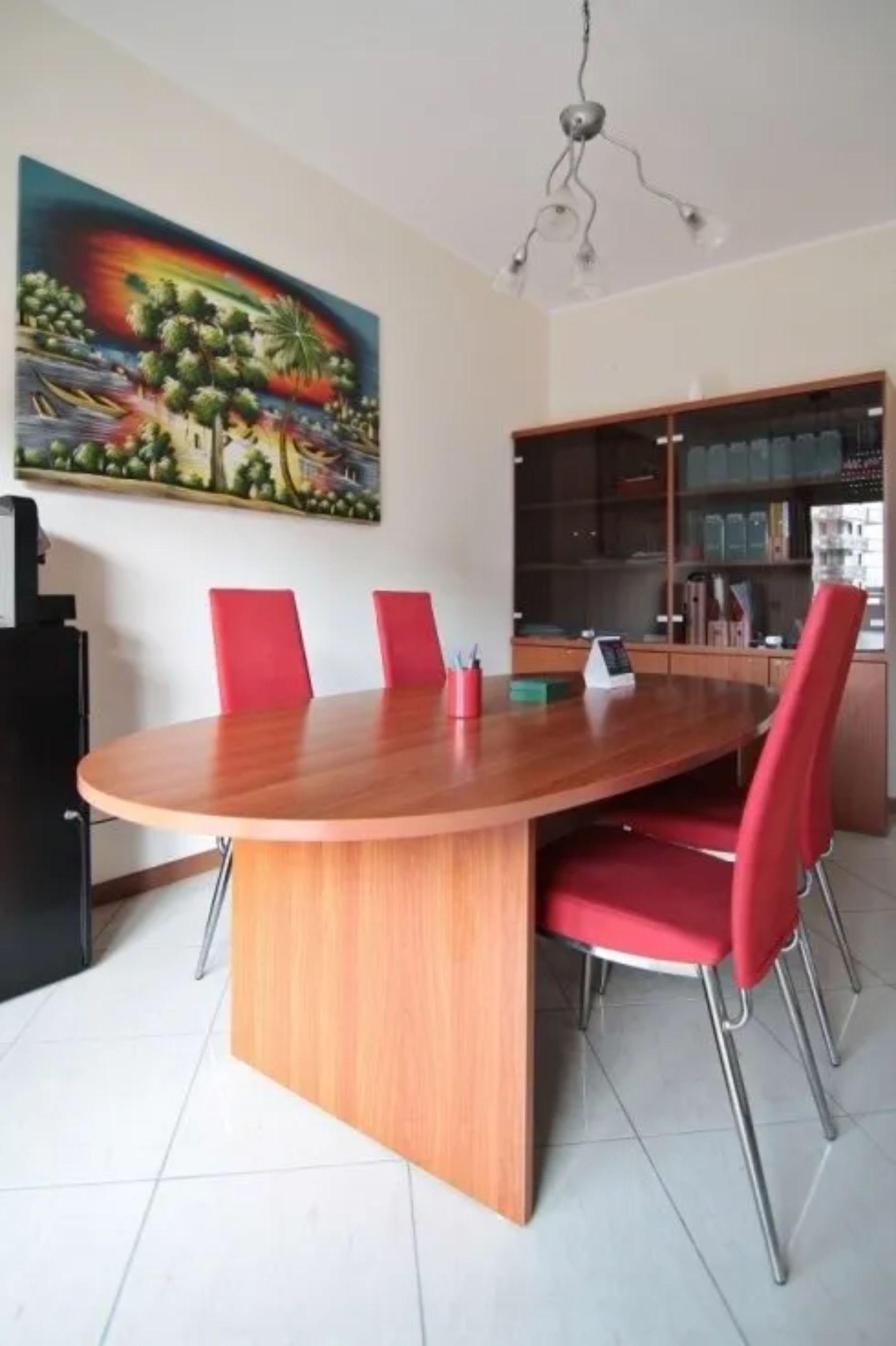 Una sala conferenze con un tavolo ovale in legno e sedie rosse. Opere d'arte appese alle pareti.