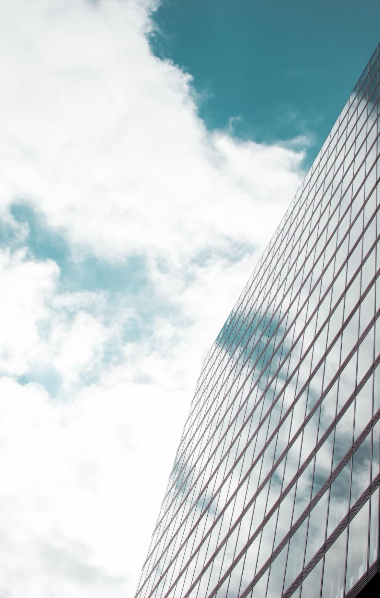 A tall building with a lot of windows against a blue sky with clouds.