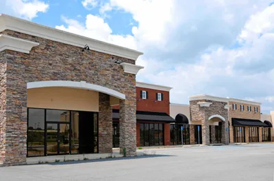 Empty strip mall with stone and stucco facades, under a partly cloudy sky.
