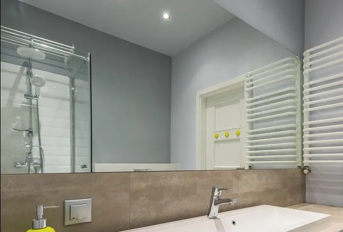 Modern bathroom with gray walls, glass shower, white towel warmers, and a sink under a mirror
