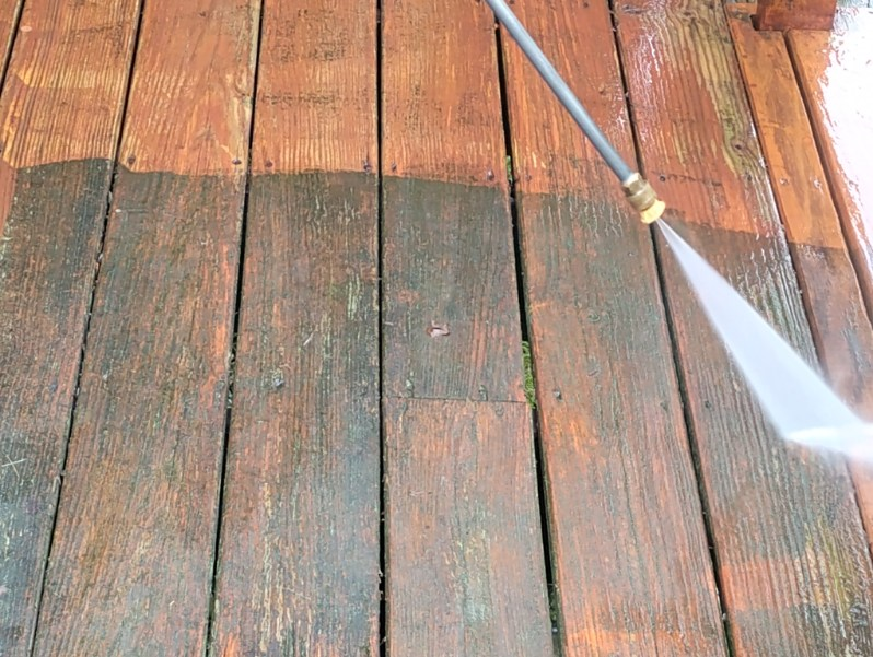 Four workers paint the exterior of a light-gray house white using paint rollers on a wooden deck.