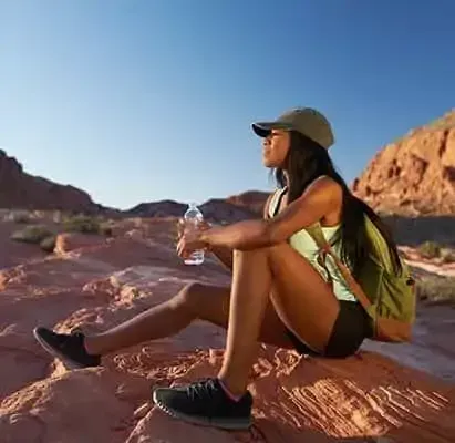 A woman is sitting on a rock in the desert holding a bottle of water.