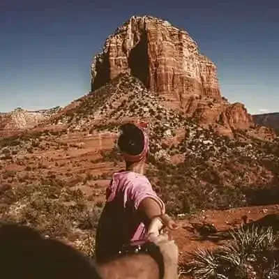 A woman is holding a man 's hand while standing in front of a mountain.
