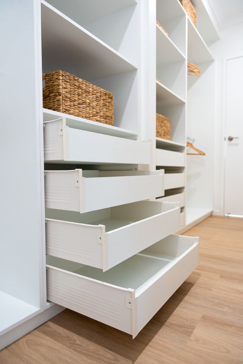 White built-in closet with open drawers and shelves holding woven baskets. Wooden floor, door visible.