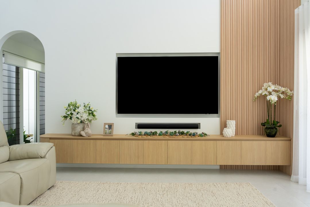 Living room with a large TV on a light wood panel, a white couch, and a cream-colored rug.