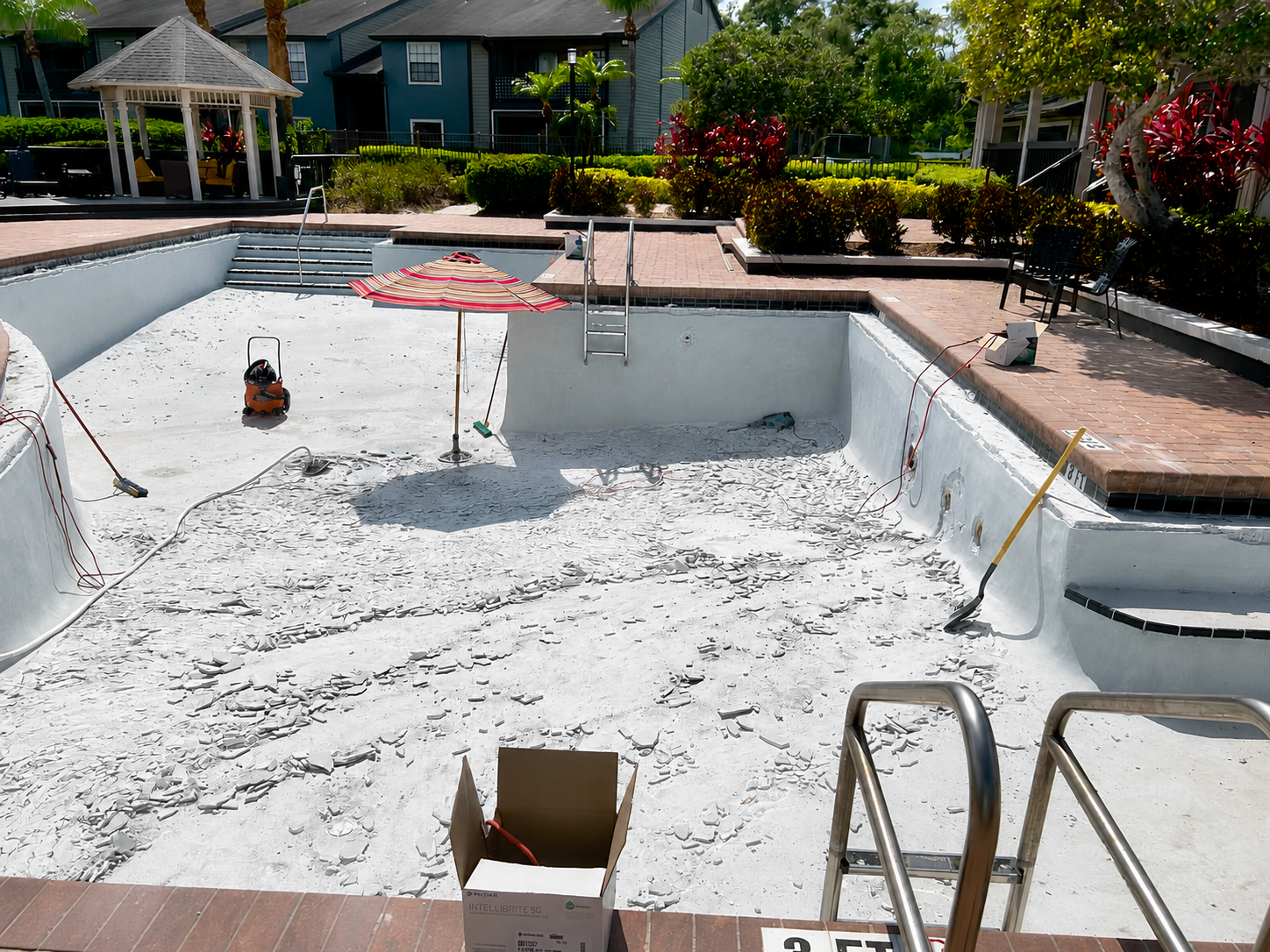 Empty drained swimming pool undergoing repair, with white coating and ladders at the edge