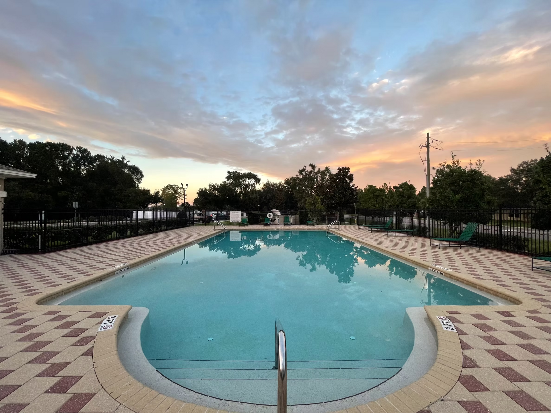 Empty outdoor swimming pool at sunset with calm water and a pastel sky.