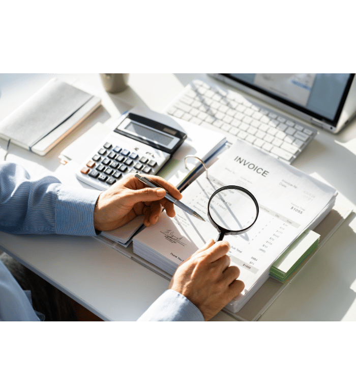 Person reviewing an invoice with a magnifying glass at a desk with calculator and keyboard