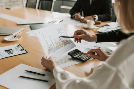 Person looking at a laptop screen with financial charts while on the phone, pointing with a pen.
