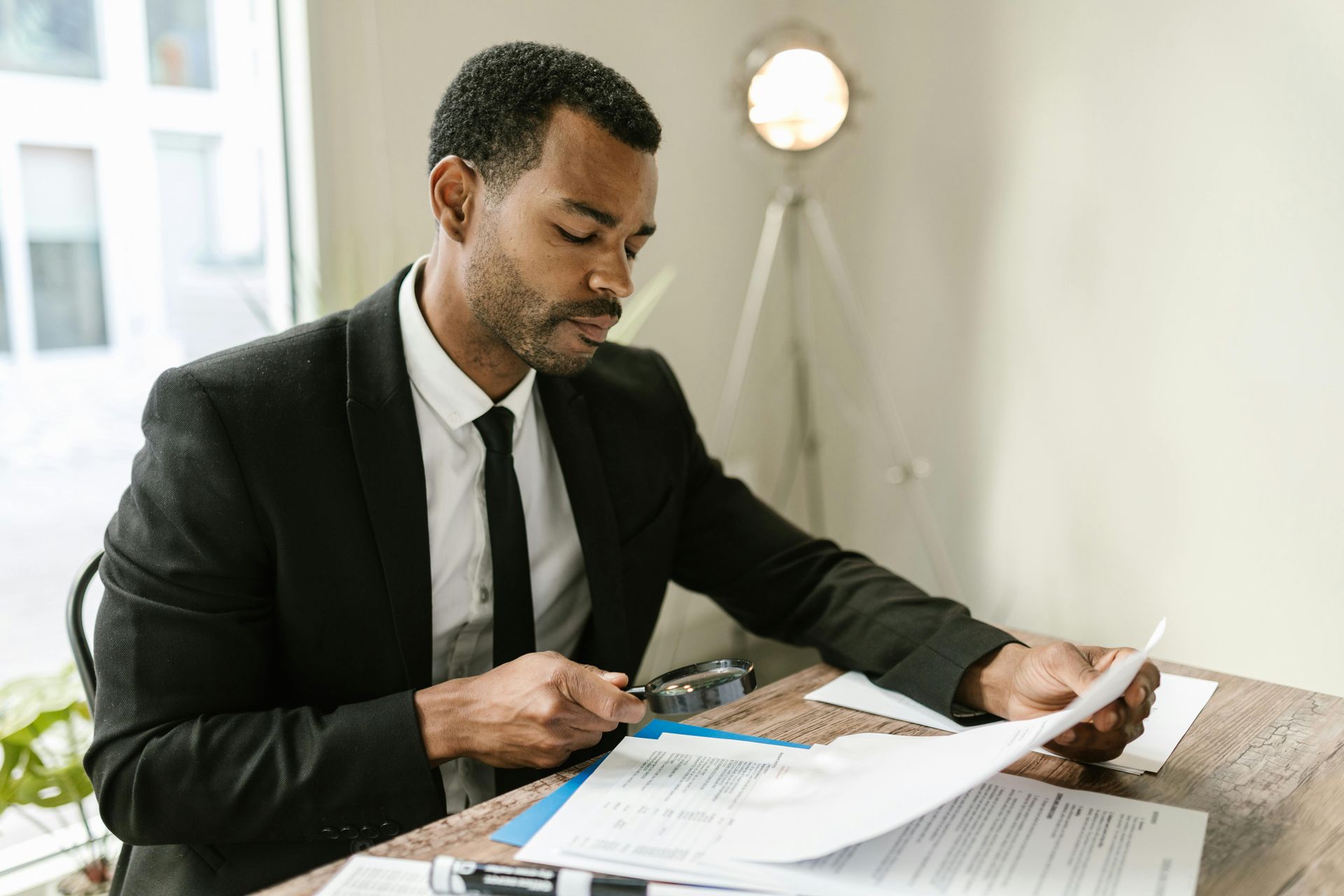 Man in a black suit reviewing papers at a desk in a bright office