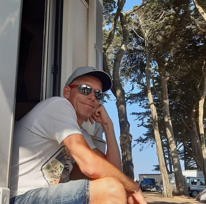 Dit is Etienne, de blije camperaar, zittend in de deuropening van zijn camper.