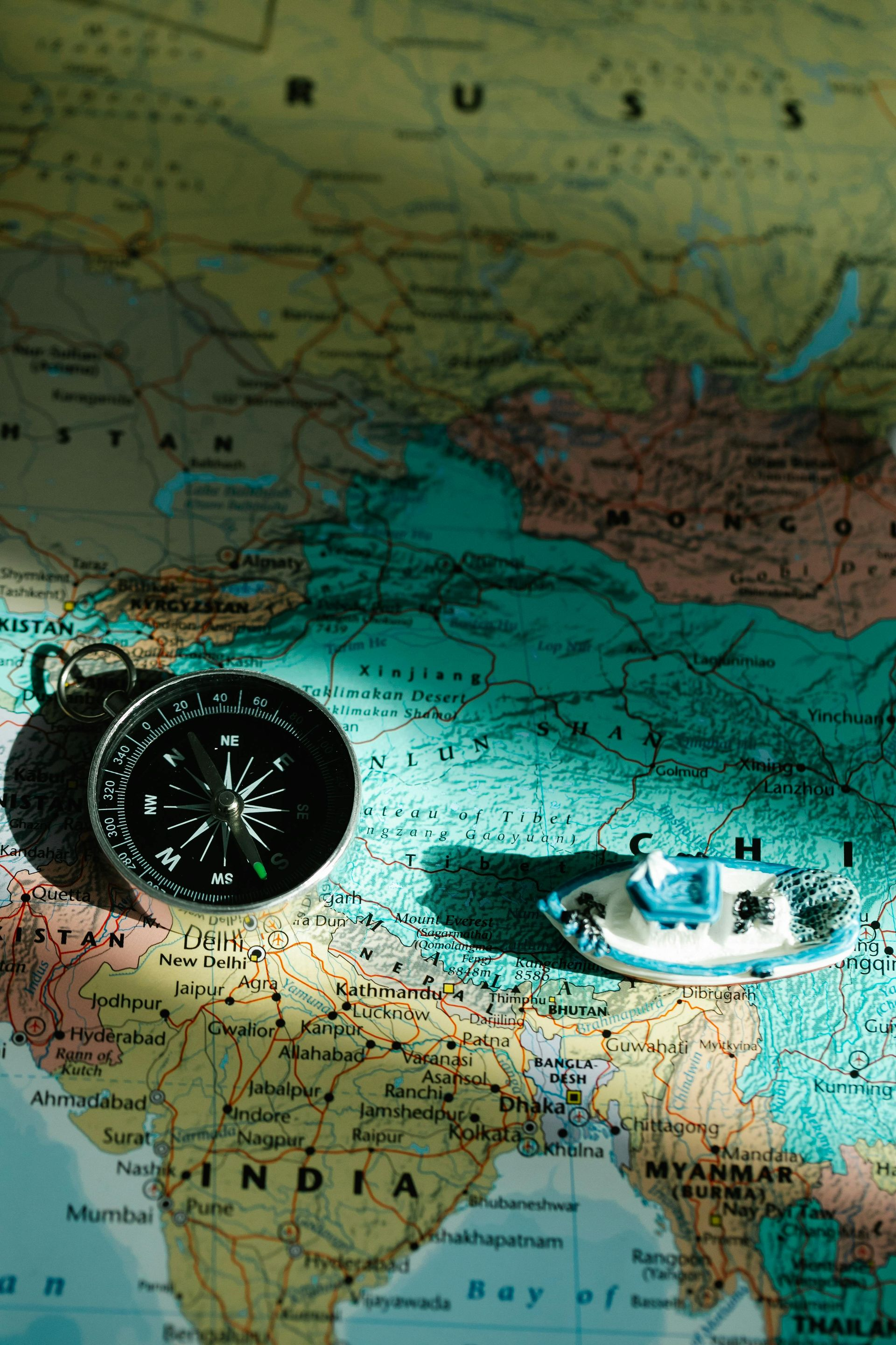 Kompas en miniatuurboot op een kaart van Azië, die schaduwen werpen.