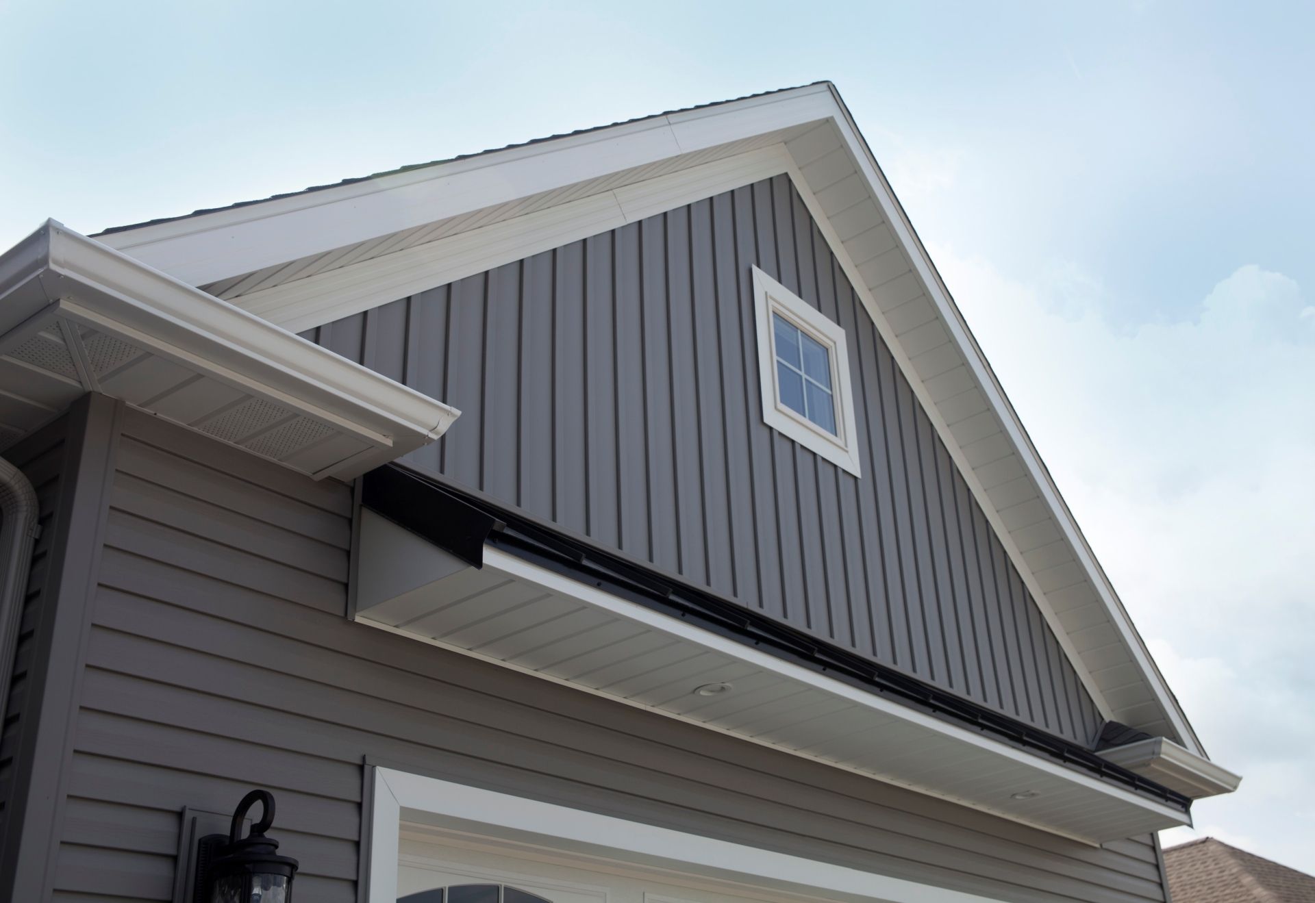 Gray house exterior with white trim, vertical siding, small window, and a dark awning.