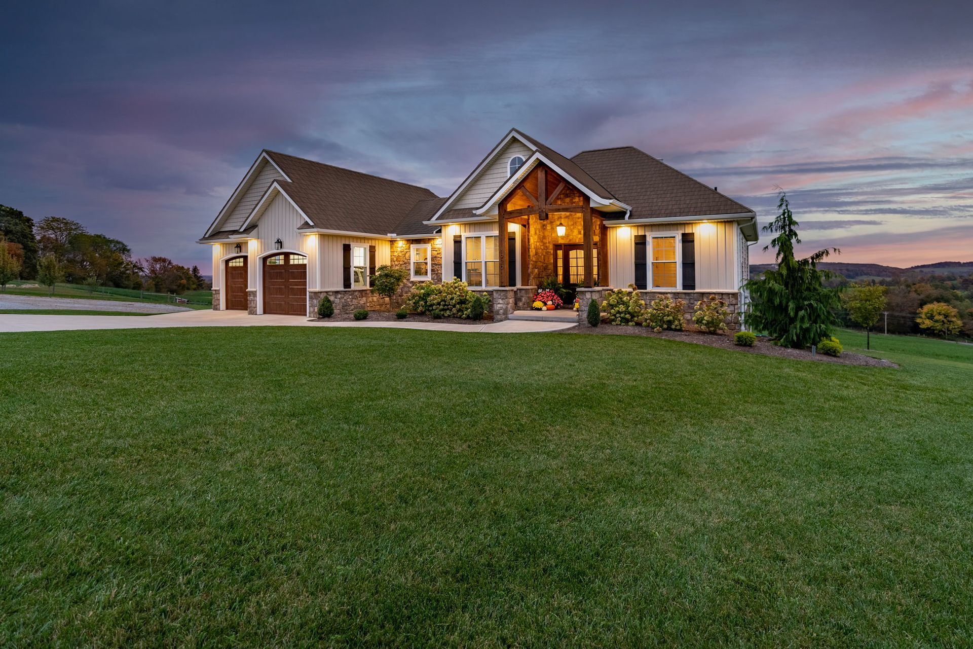 House with stone and wood accents, two-car garage, and lush green lawn at dusk.