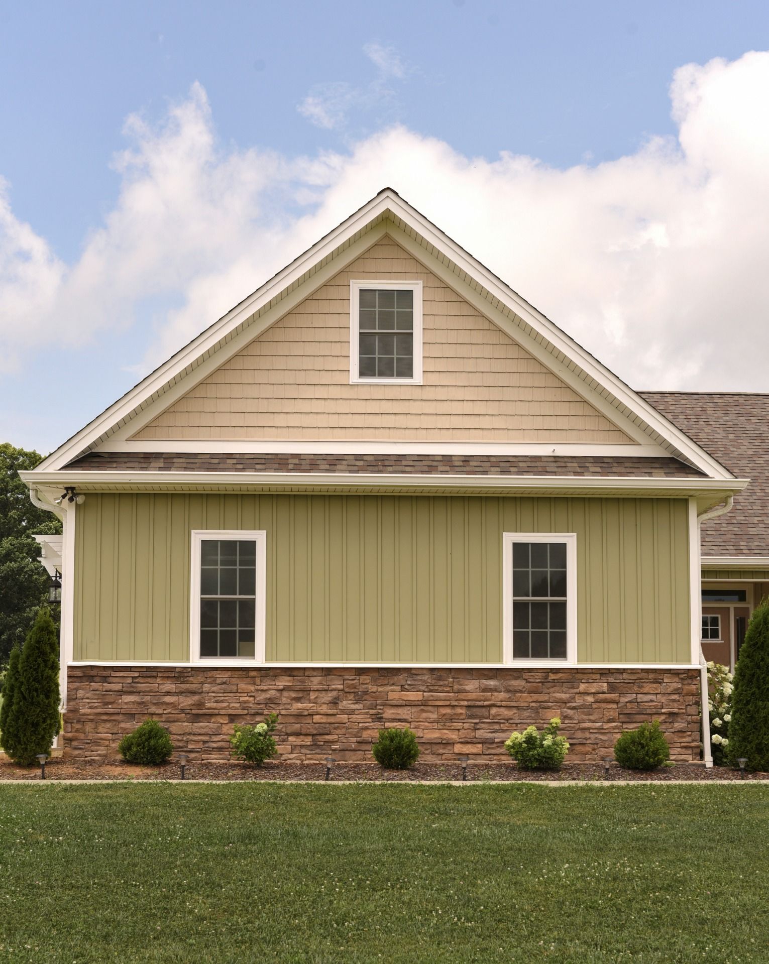 Green house with stone base, gable roof, and two windows.