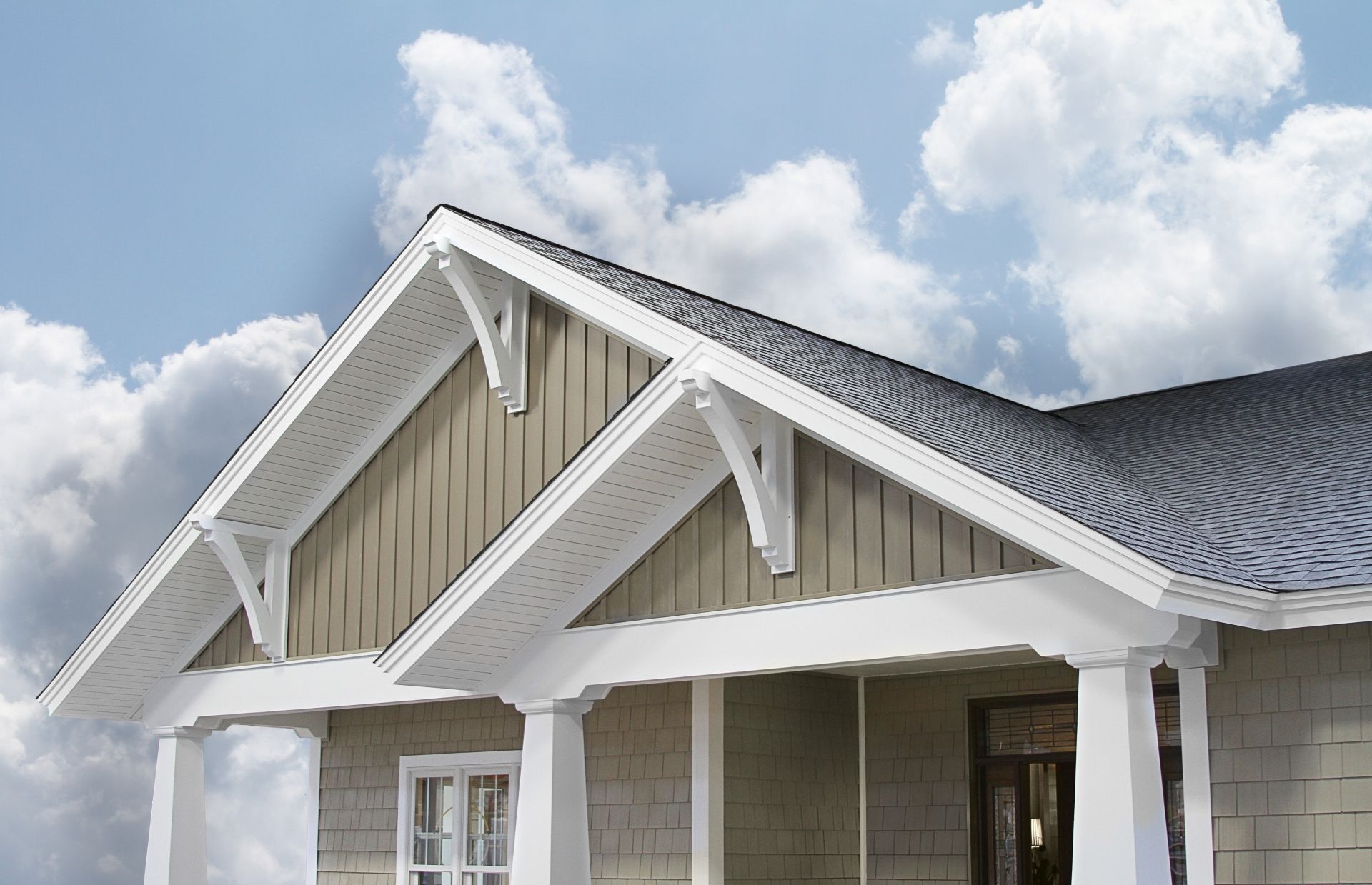 Beige house with gabled roof, white trim, and decorative brackets against a cloudy sky.