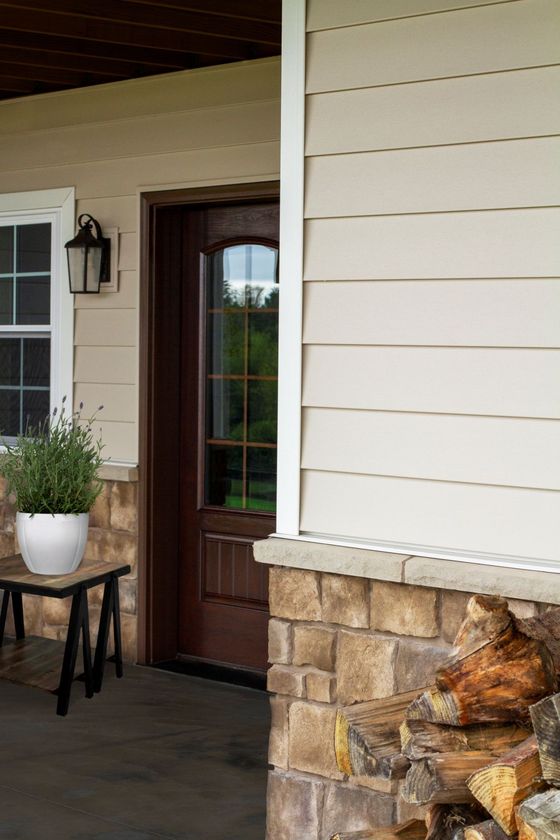 Exterior of a home with a wooden door, stone base, beige siding, and a small potted plant.