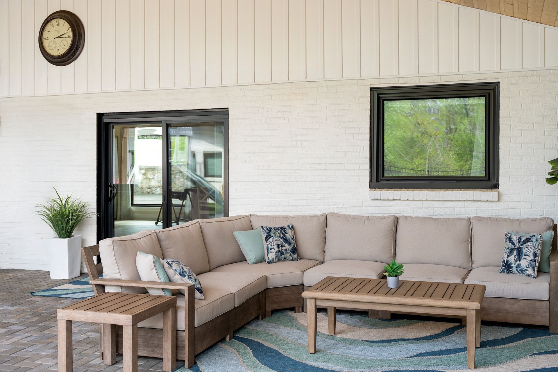 Outdoor sectional seating on a patio with a coffee table, rug, and window.