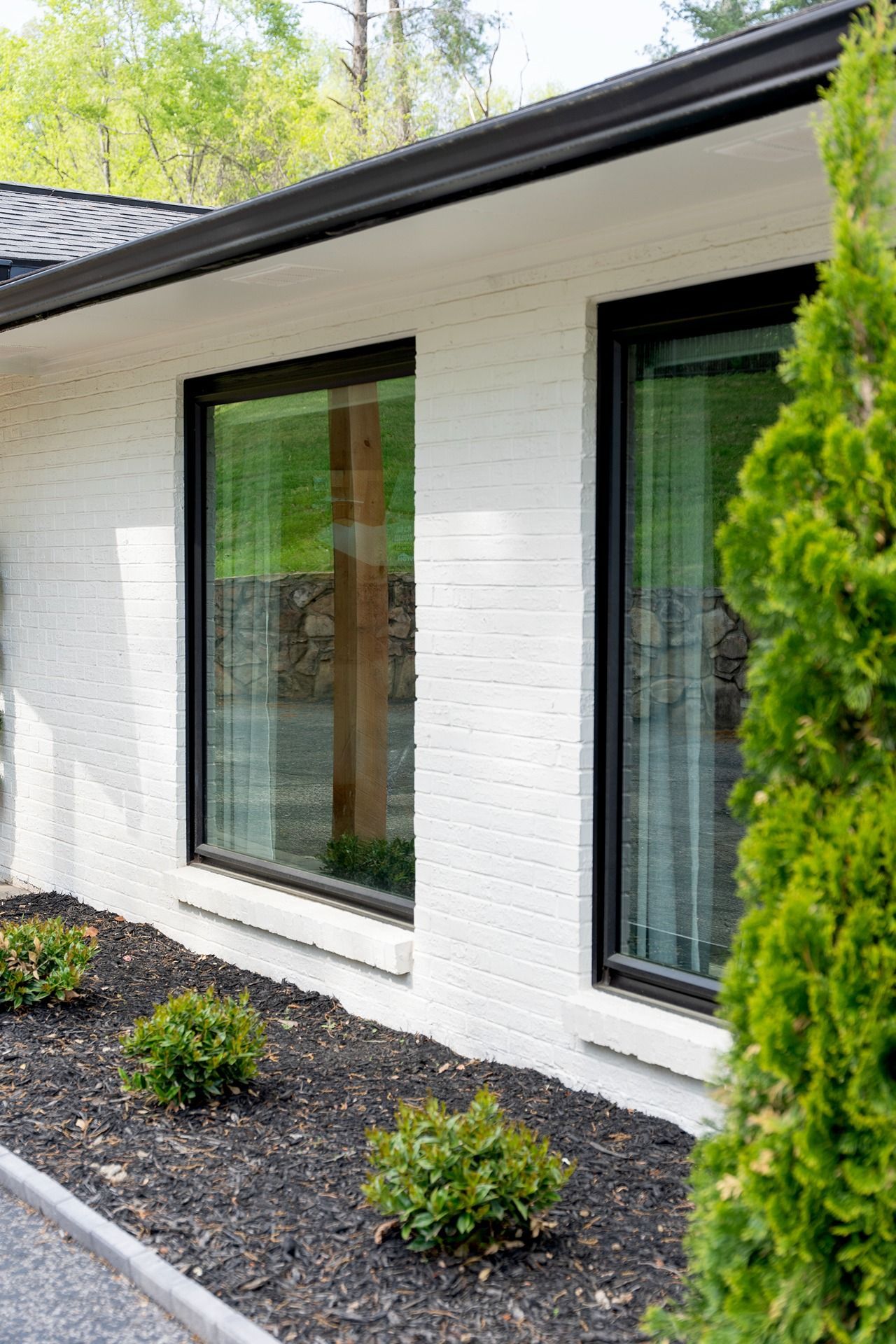 White brick building with black-framed windows; dark mulch and green shrubs in foreground.
