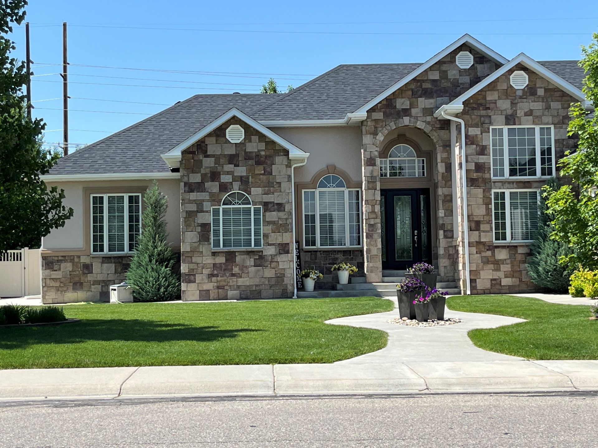 House with stone facade, dark roof, arched entryway, and well-manicured lawn on a sunny day.