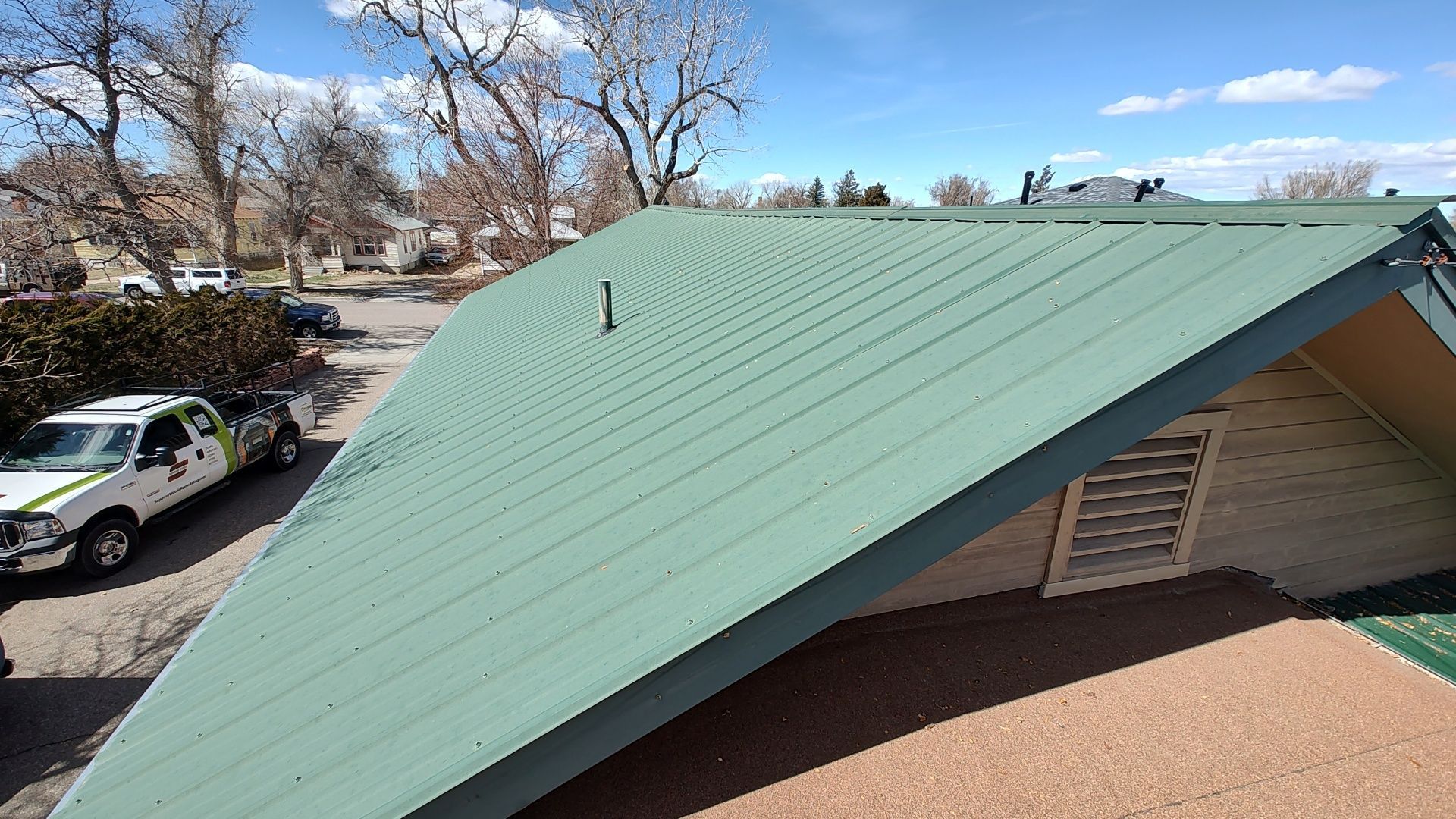 Green metal roof on a building, angled toward the viewer; a parked truck is visible.