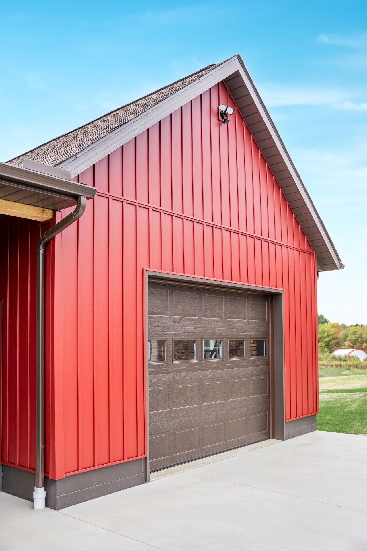 Red metal-sided garage with brown trim, door, and roof. Blue sky in the background.