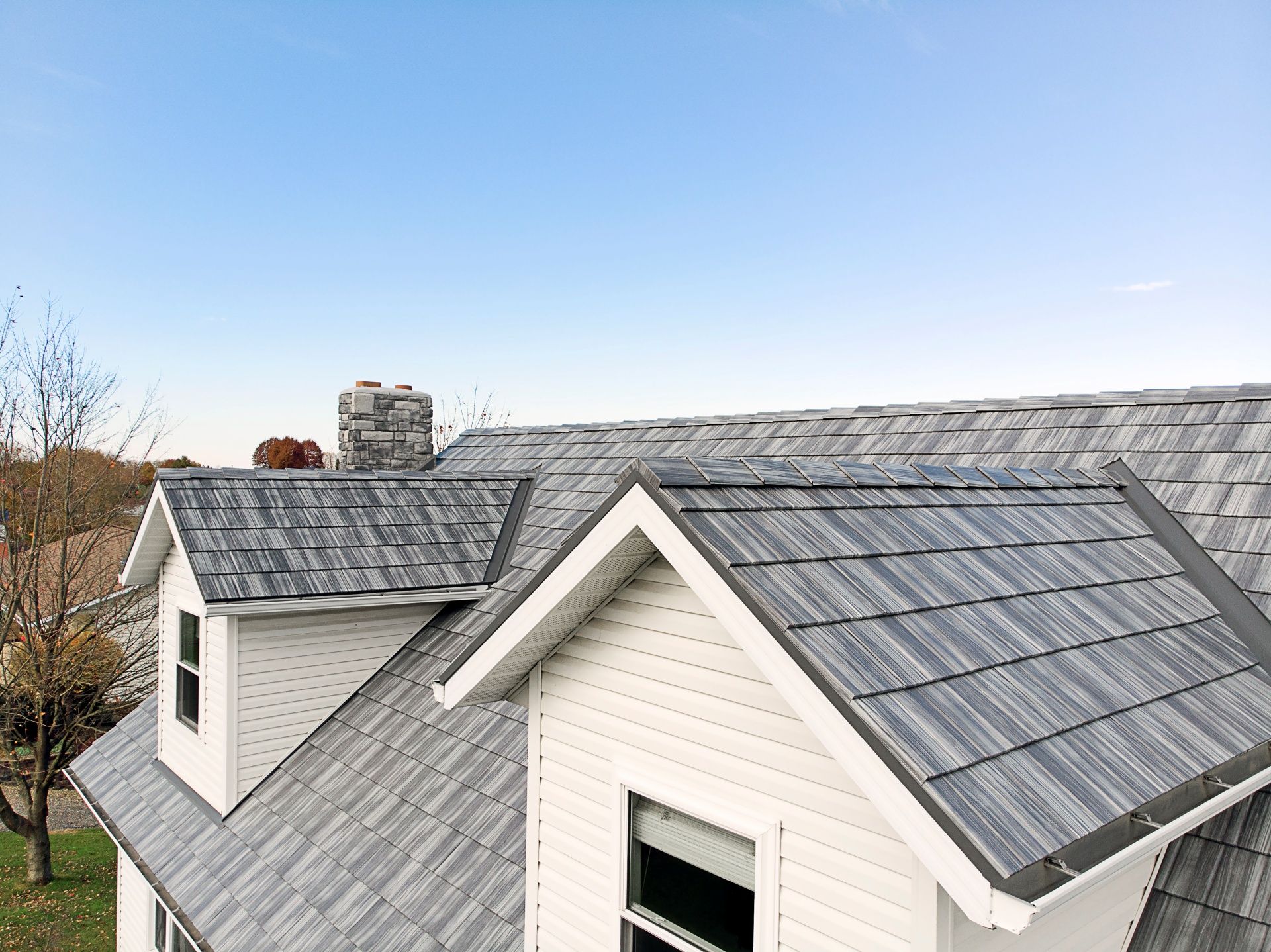 Gray and white house roof with dormers, chimney, and blue sky.